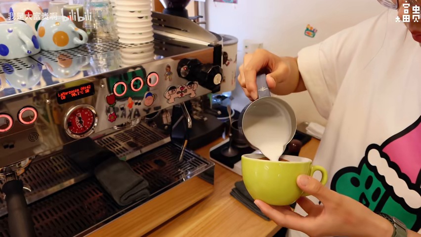A barista pours milk into a green cup